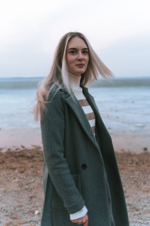 Free A fashionable woman in a green coat enjoying a peaceful lakeside view. Stock Photo