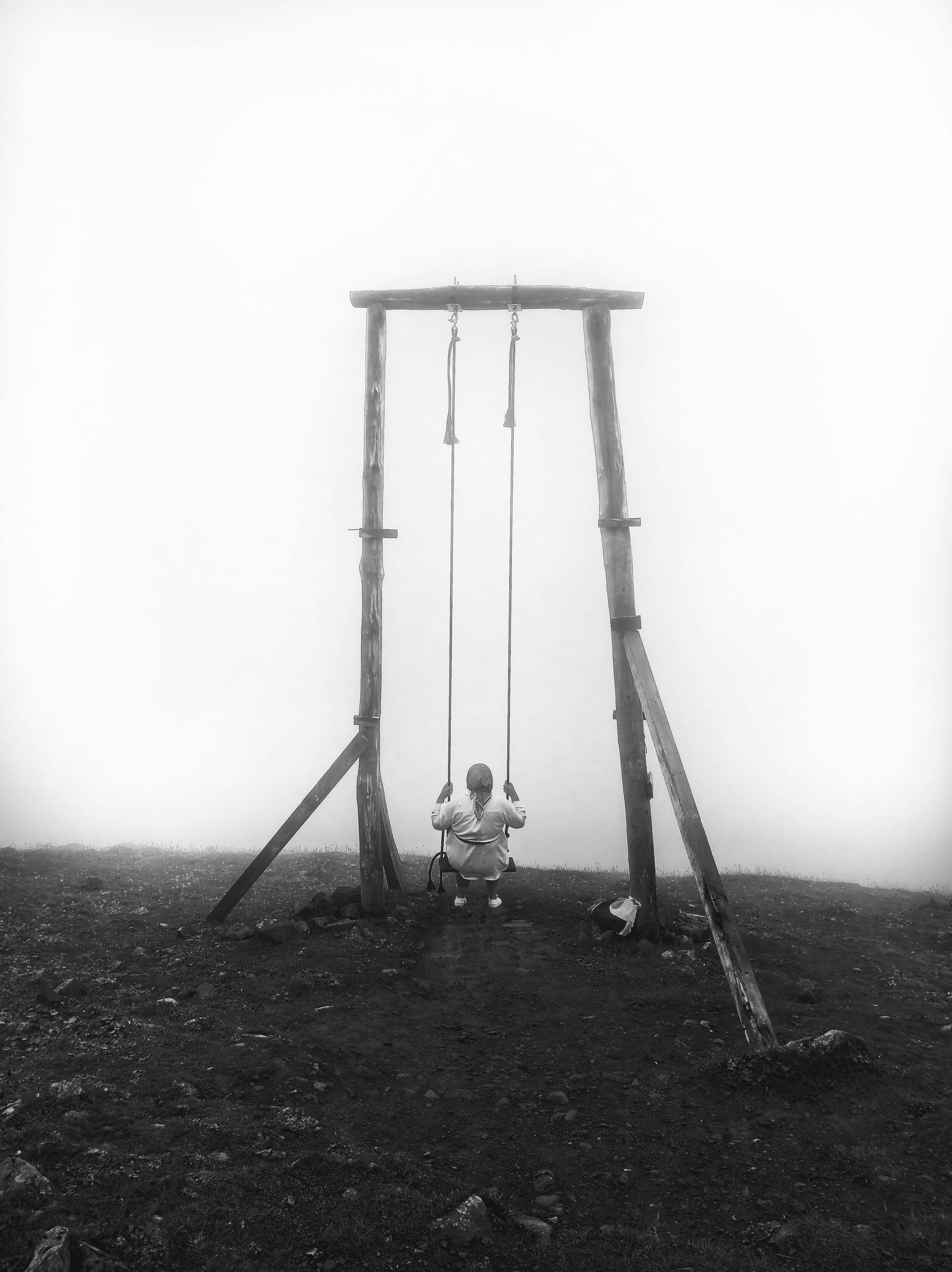 A lone person on a swing set in a foggy outdoor setting exudes solitude.