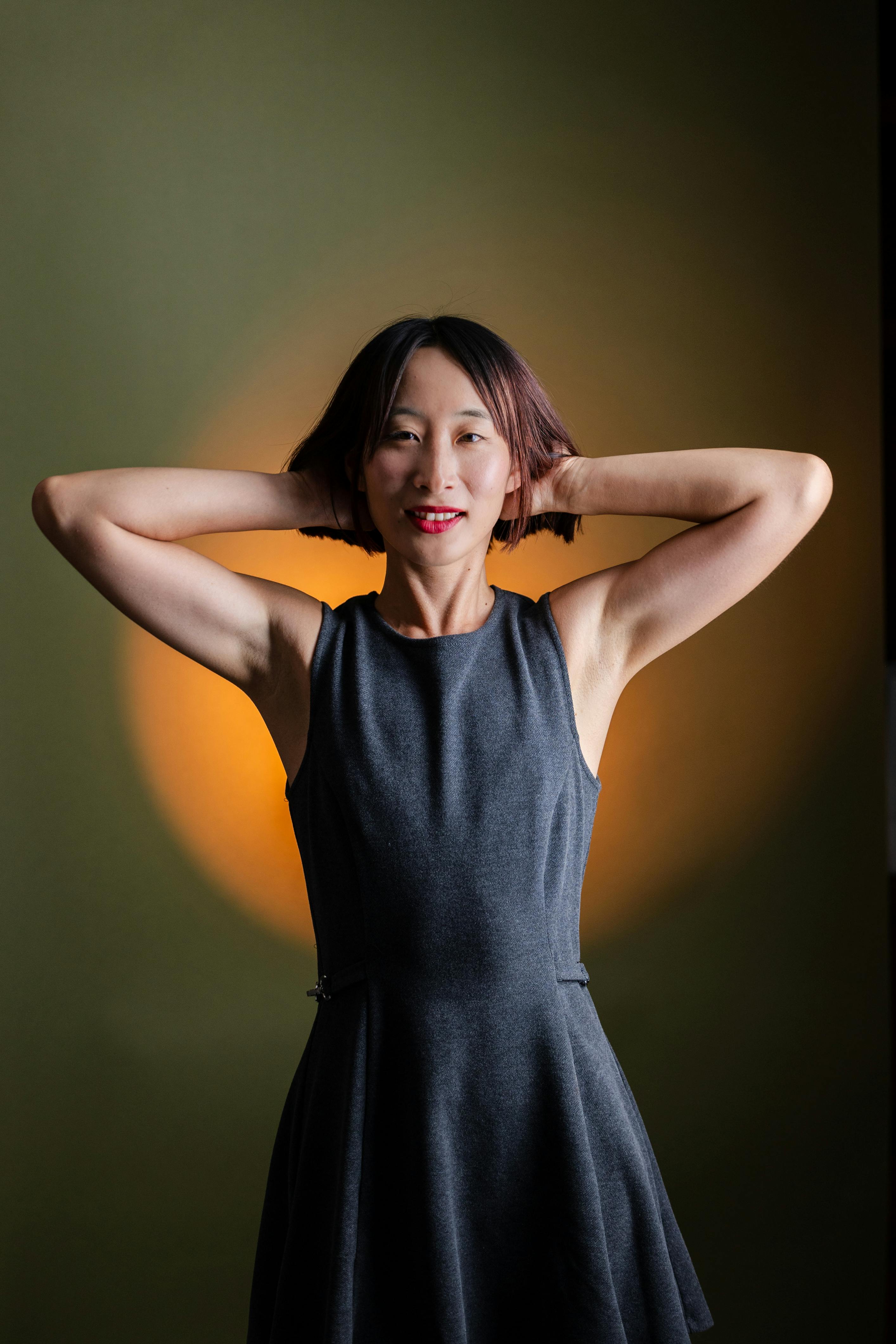 A serene studio portrait of a woman in a stylish dress with arms raised against a colorful backdrop.