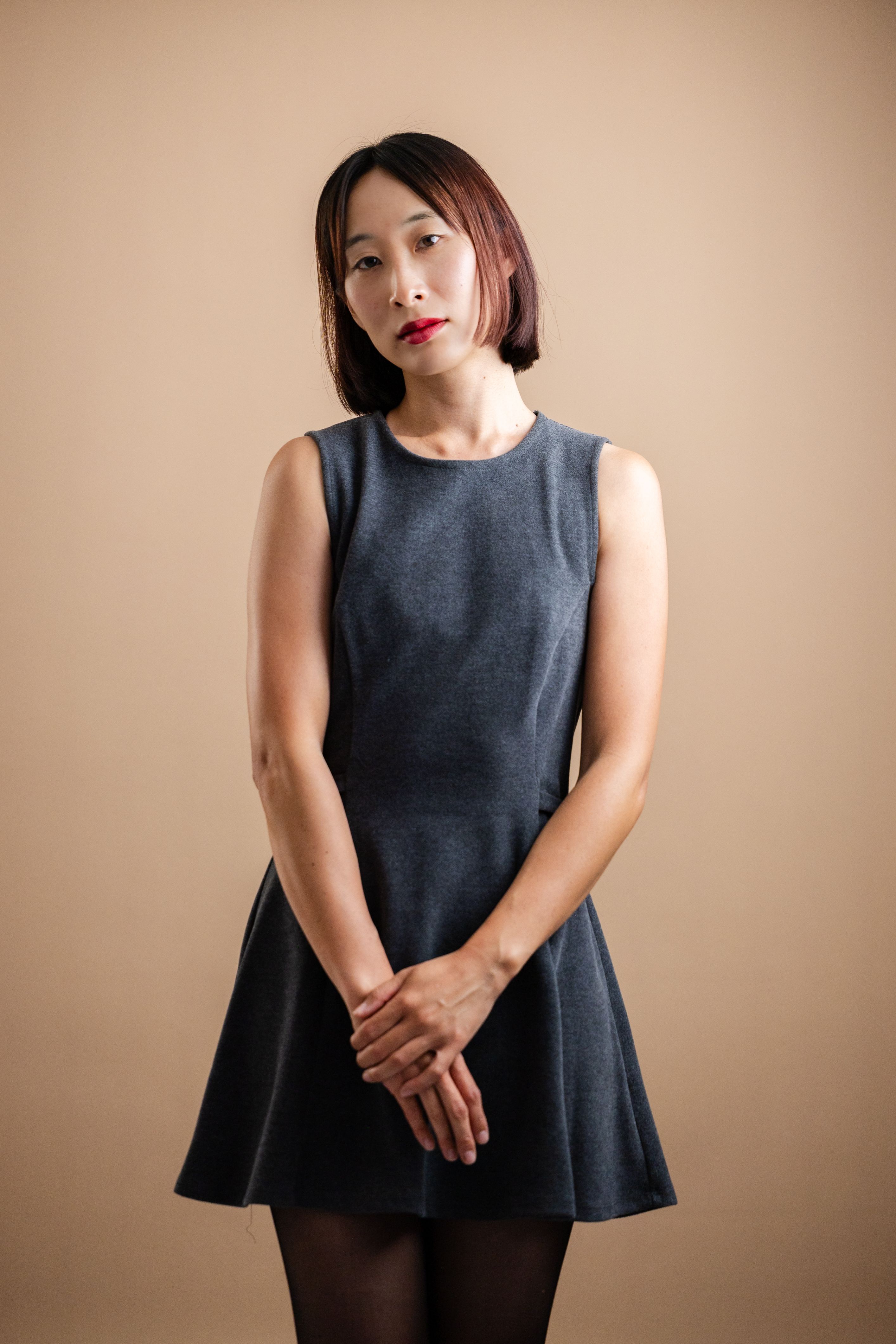 Portrait of a woman in a minimalist dress against a neutral background, exuding elegance.