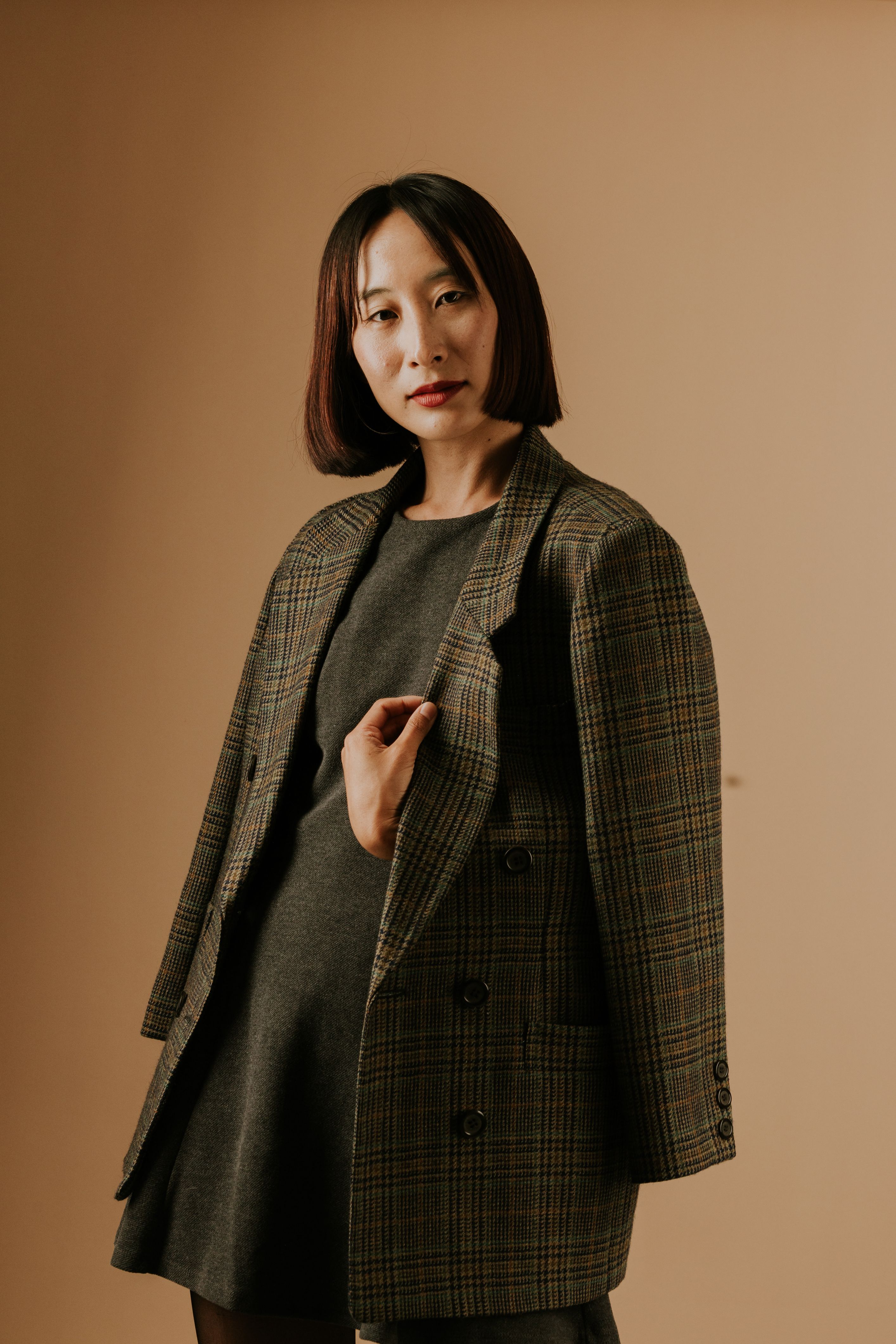Stylish portrait of an adult woman wearing a plaid jacket, posing confidently against a neutral backdrop.