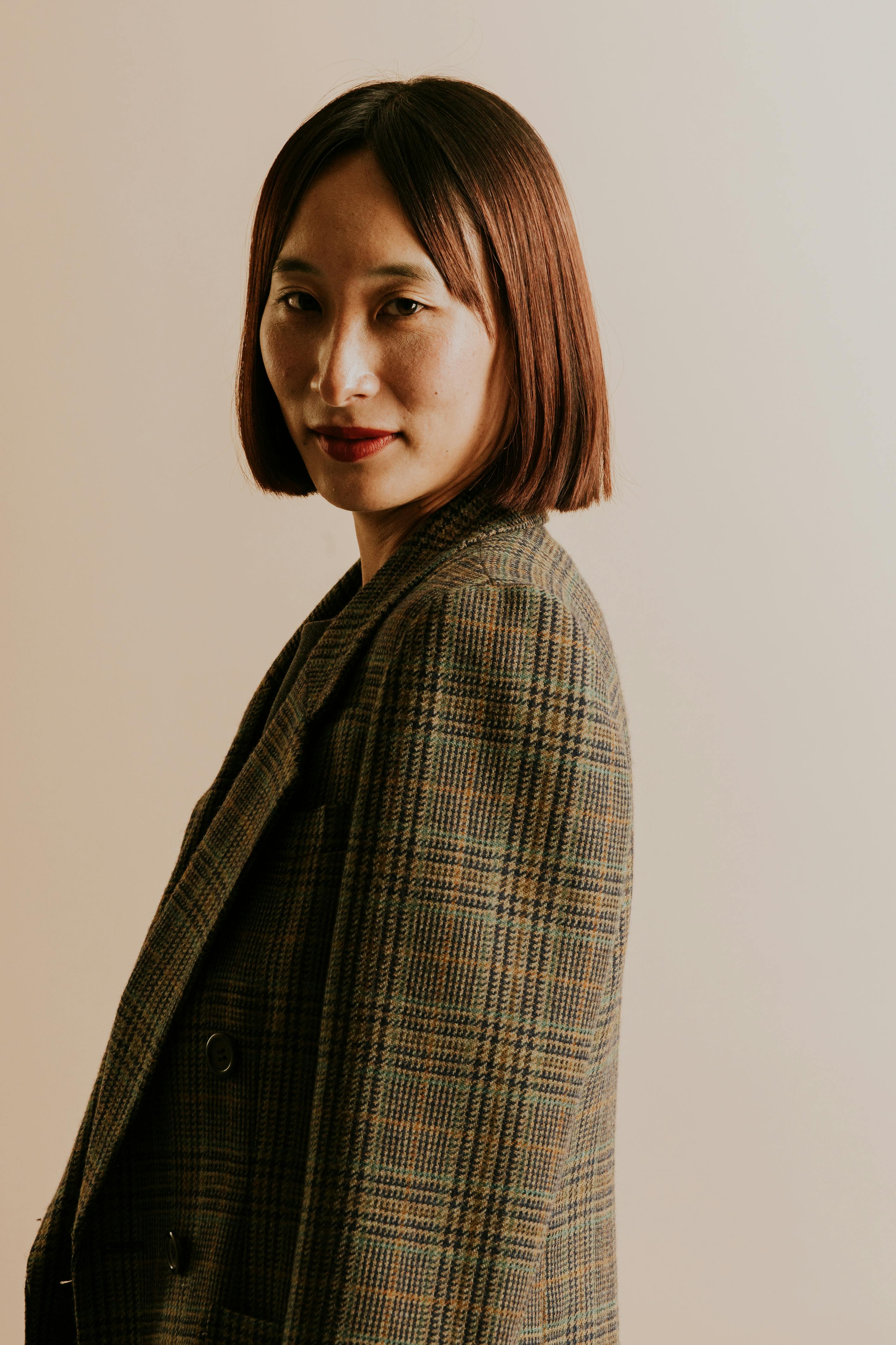 Stylish portrait of a woman wearing a plaid blazer with a neutral background.