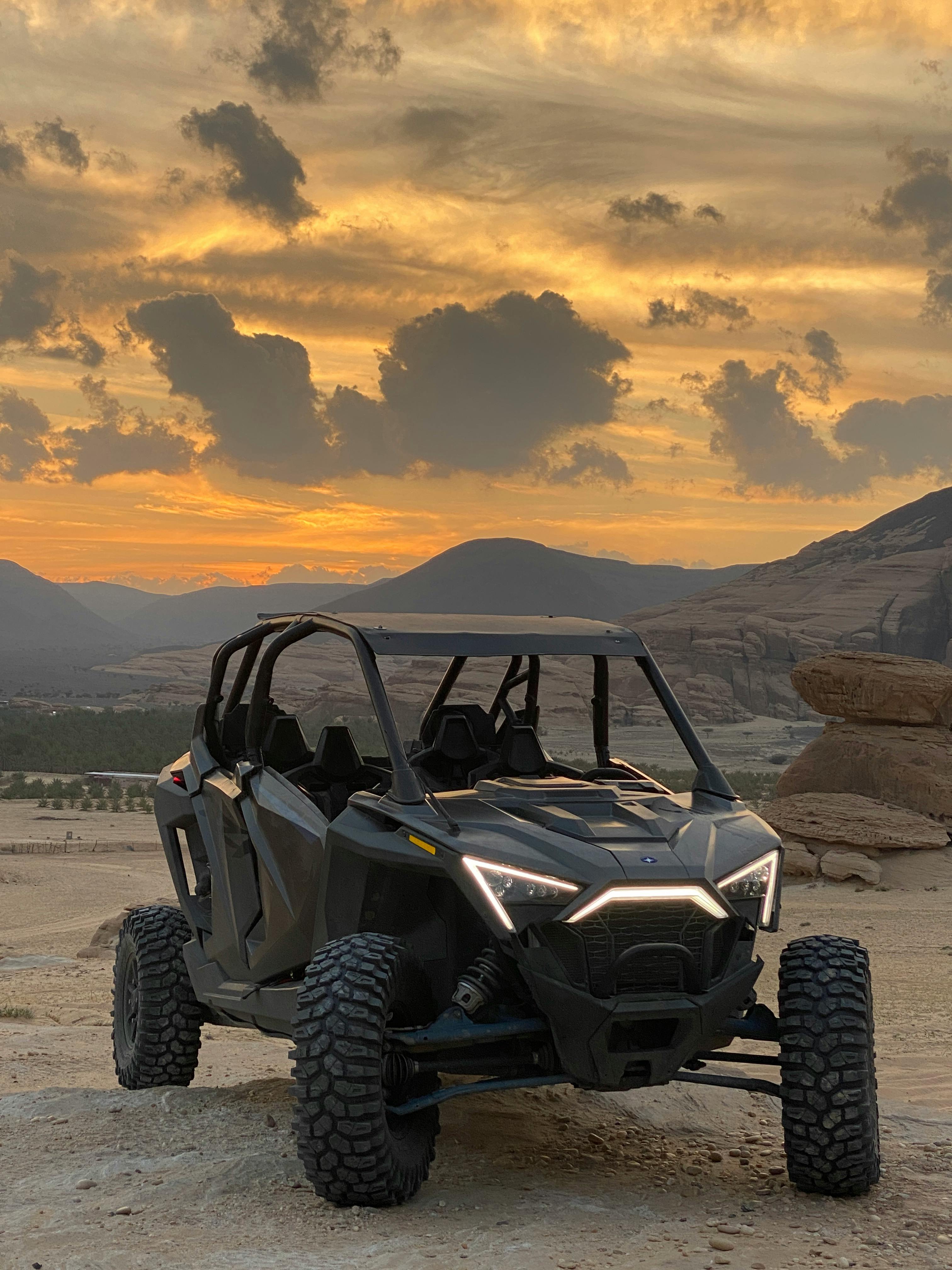 An off-road vehicle parked against a stunning sunset backdrop in a desert landscape.