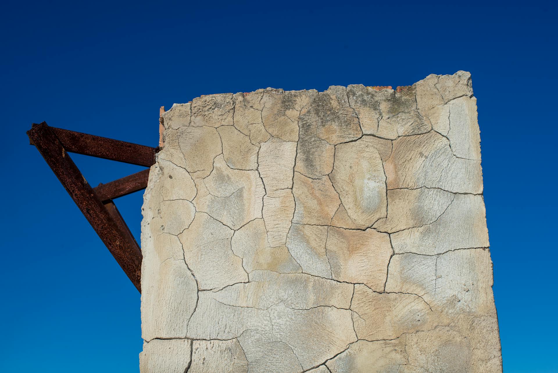 A weathered wall with cracks stands out against a vibrant blue sky, showcasing decay and resilience.