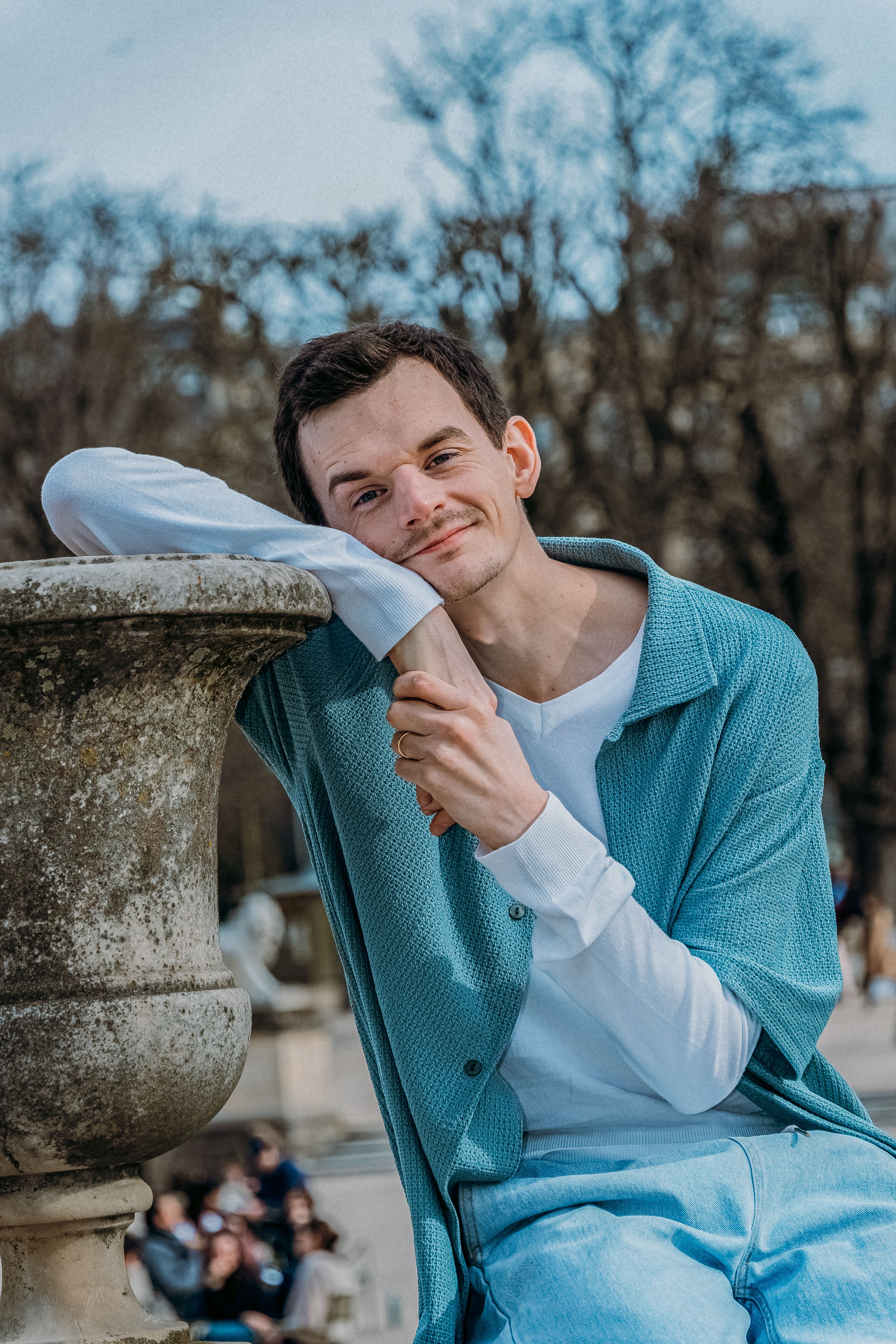 Stylish young man with light blue outfit enjoying a sunny day in a Paris park.