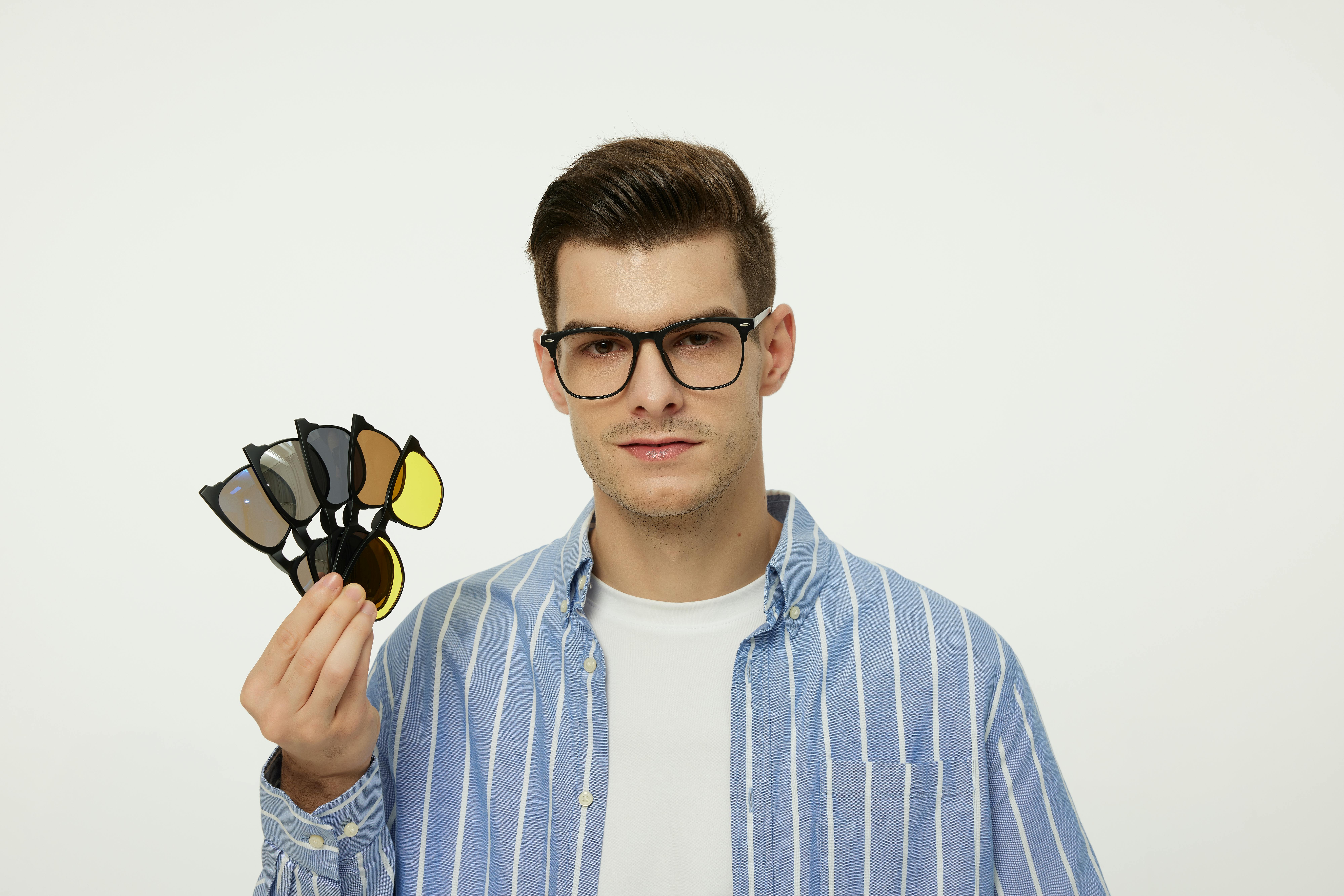 Free Fashionable young man with glasses holding a set of interchangeable lenses for a stylish look. Stock Photo