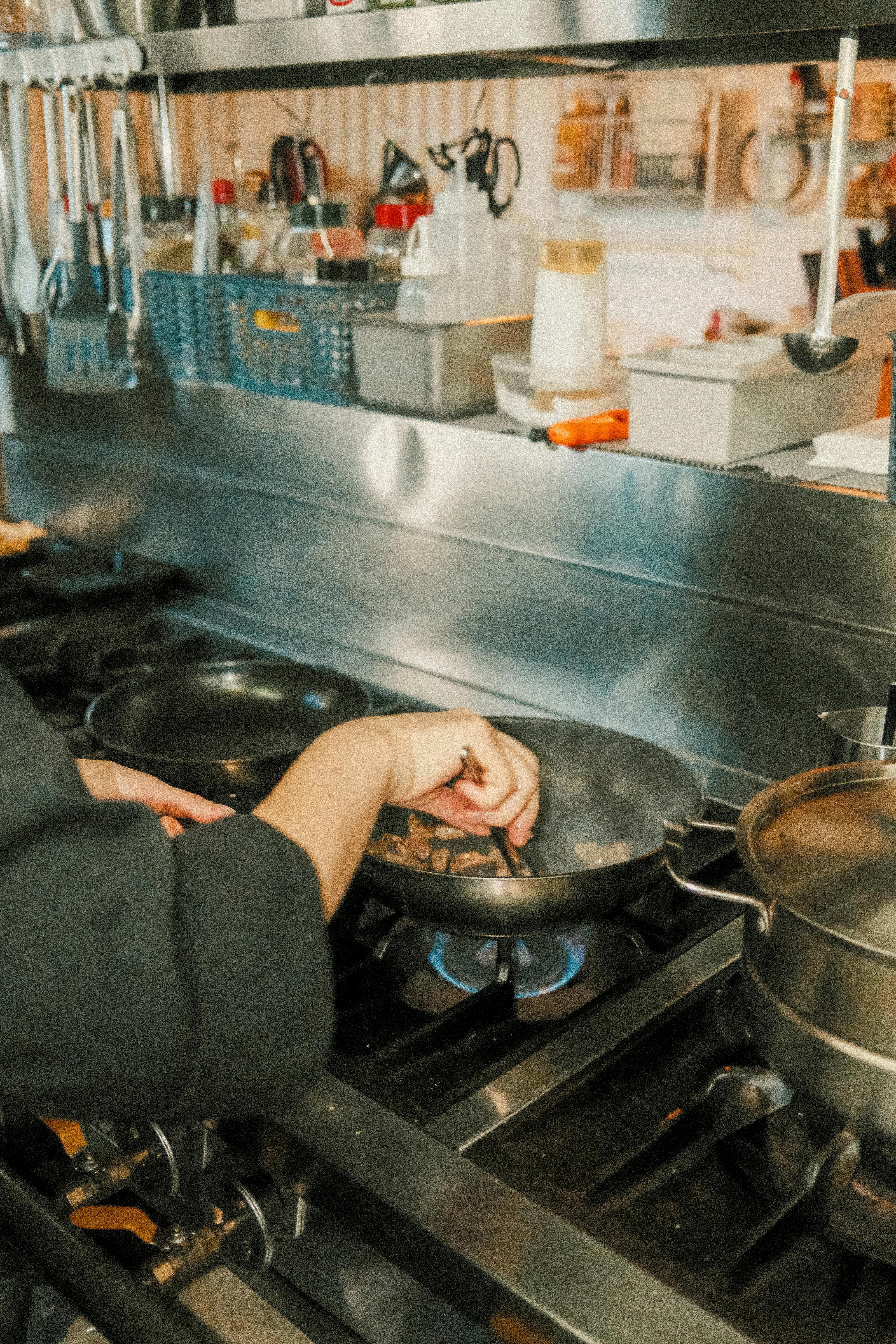 Chef cooking on a gas stove in a busy professional kitchen setting.