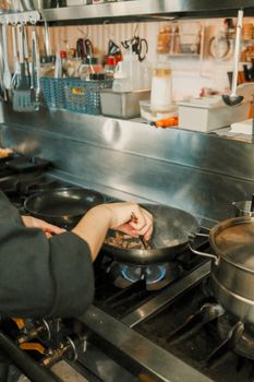 Chef cooking on a gas stove in a busy professional kitchen setting.