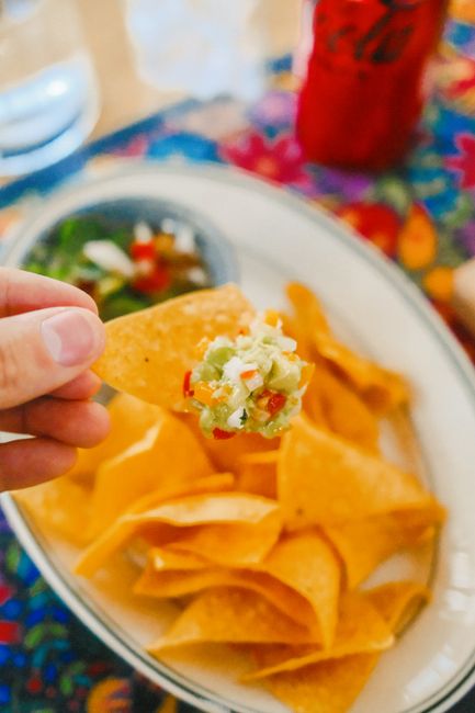 Hand holding nacho chip with guacamole. Bright and colorful composition.