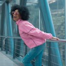 一位卷发、身穿粉色夹克、戴着太阳镜的女人在室内微笑着享受片刻时光