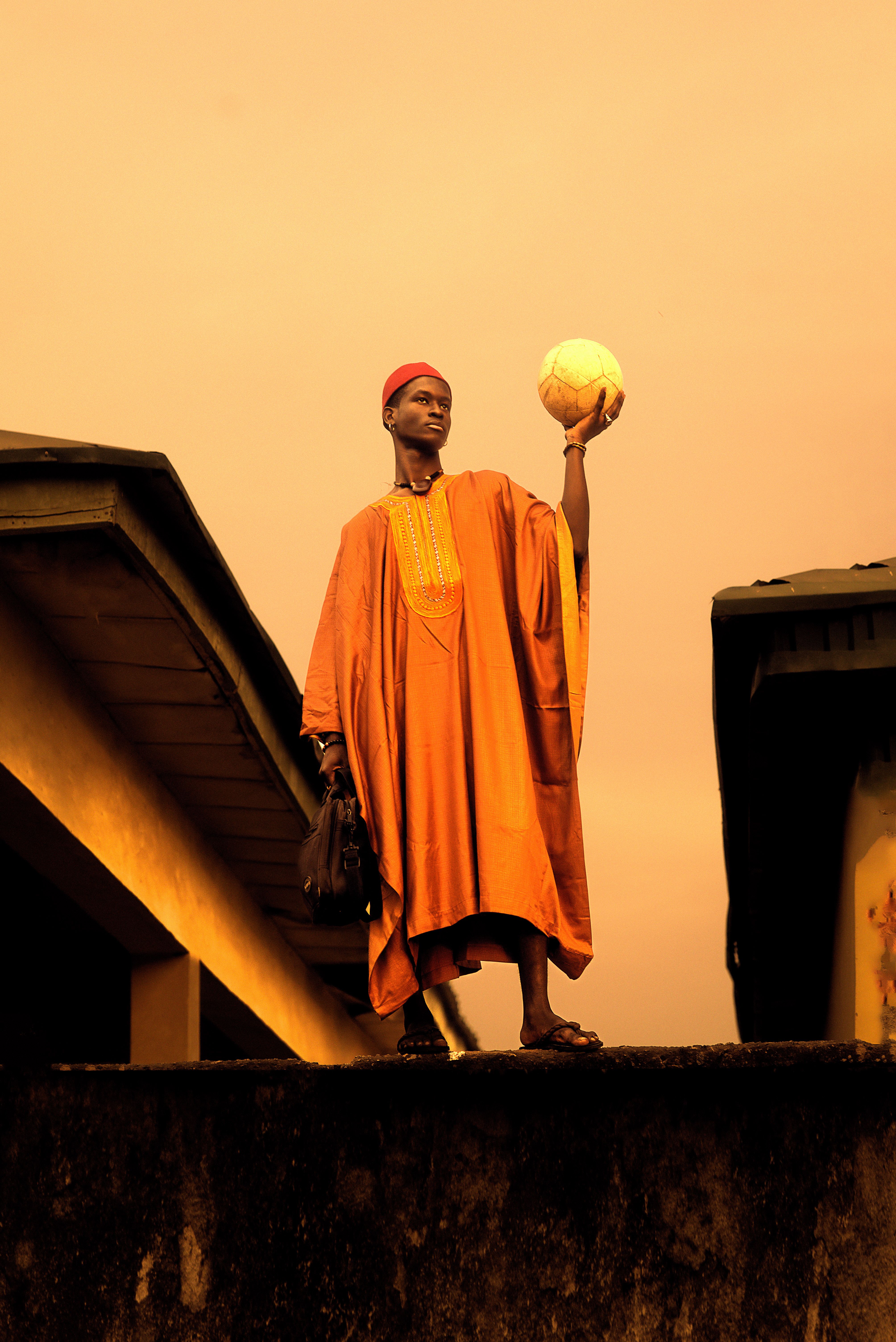Man in traditional garment holding a ball, silhouetted against a sunset sky.
