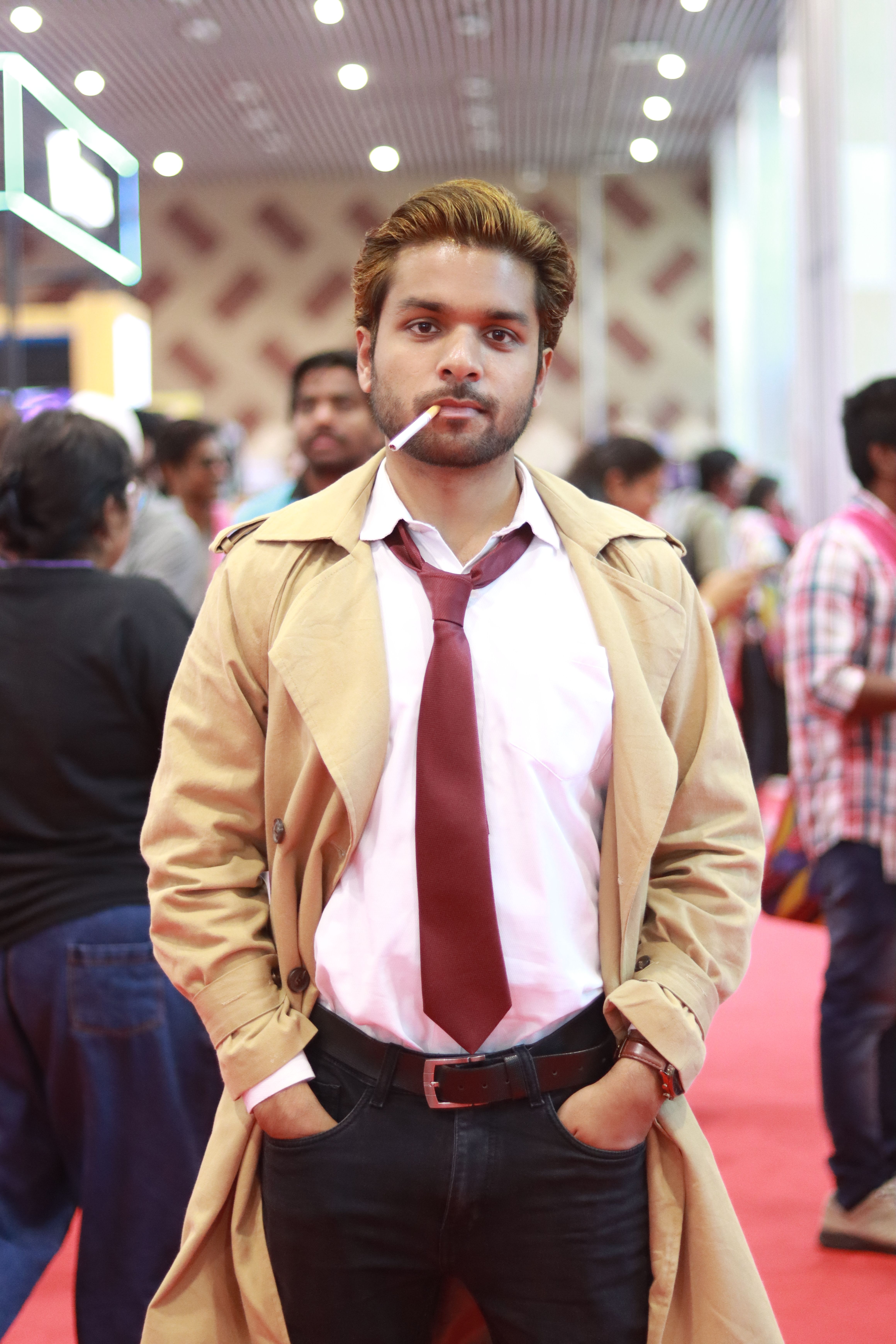 Young man dressed in cosplay with trench coat and cigarette, standing confidently at a convention.