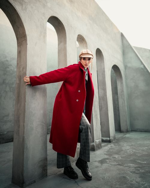 Free Stylish woman in a red coat posing against modern architecture with arched walls. Stock Photo