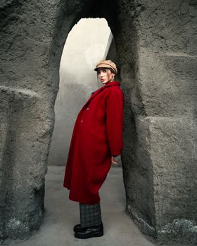 Stylish woman in a red coat posed in a rugged stone archway, showcasing modern fashion.