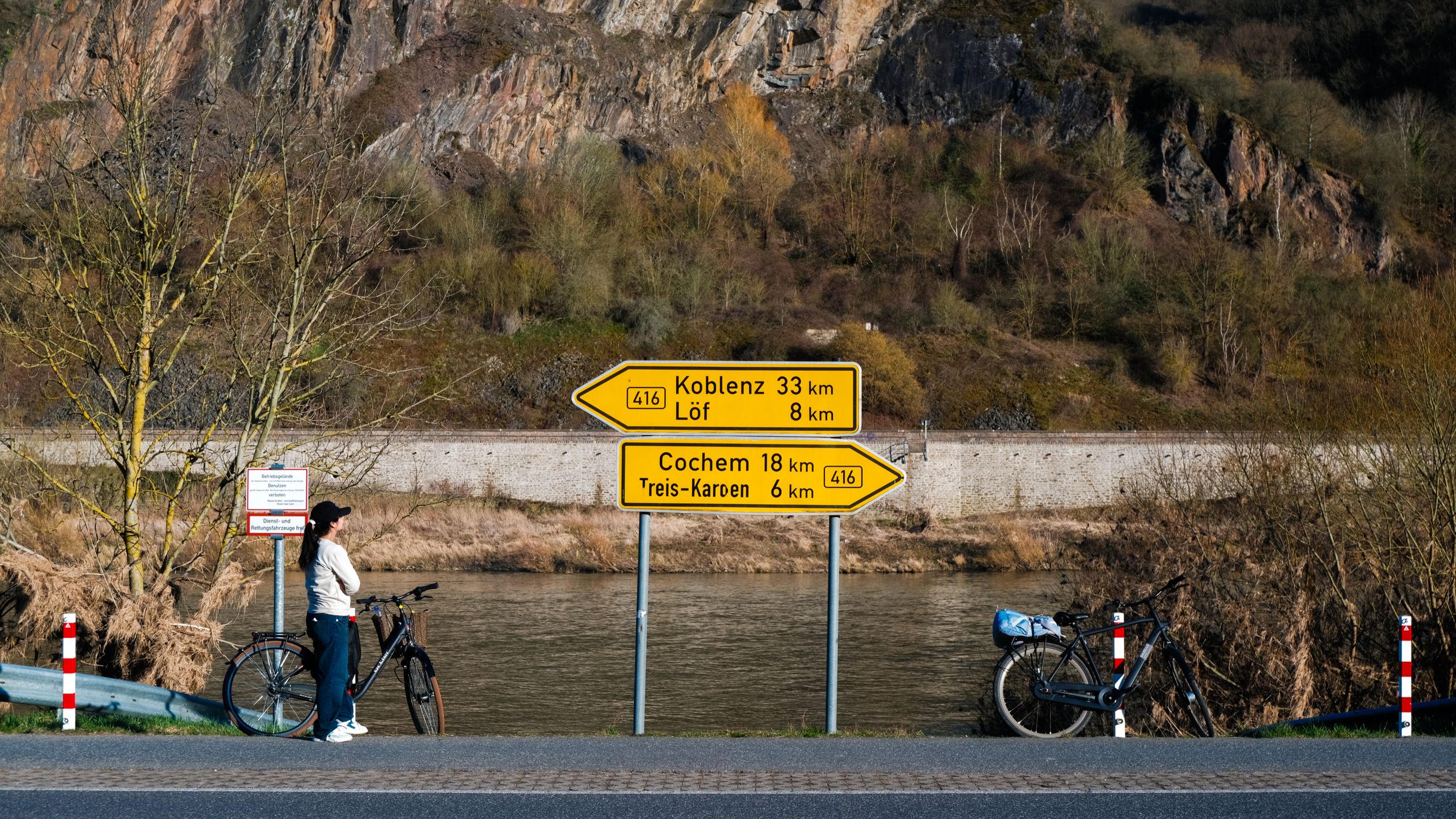 Cyclist pauses beside a road sign pointing towards Koblenz and Cochem in scenic German landscape.
