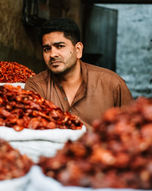 Free Serious adult ethnic male vendor in casual shirt sitting at stall with colorful authentic goods and looking at camera while working on local market Stock Photo