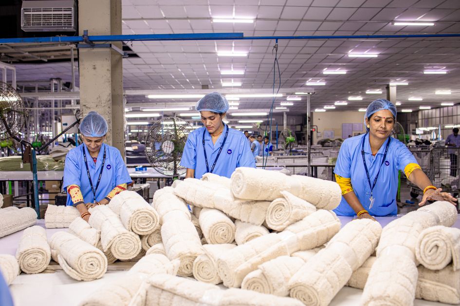 Công nhân trong nhà máy dệt may đang cuộn và sắp xếp các cuộn vải trắng trên bàn thao tác