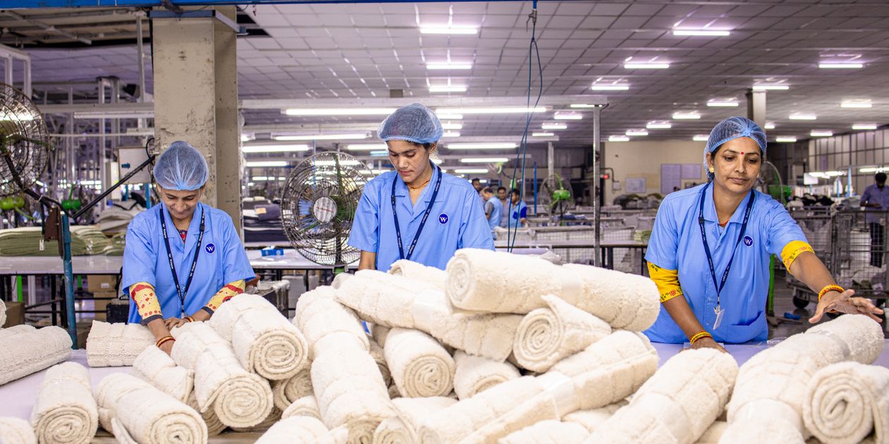 Công nhân trong nhà máy dệt may đang cuộn và sắp xếp các cuộn vải trắng trên bàn thao tác