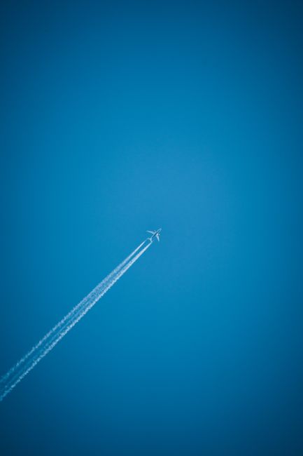 Airplane soaring high, leaving a contrail against a vibrant blue sky.