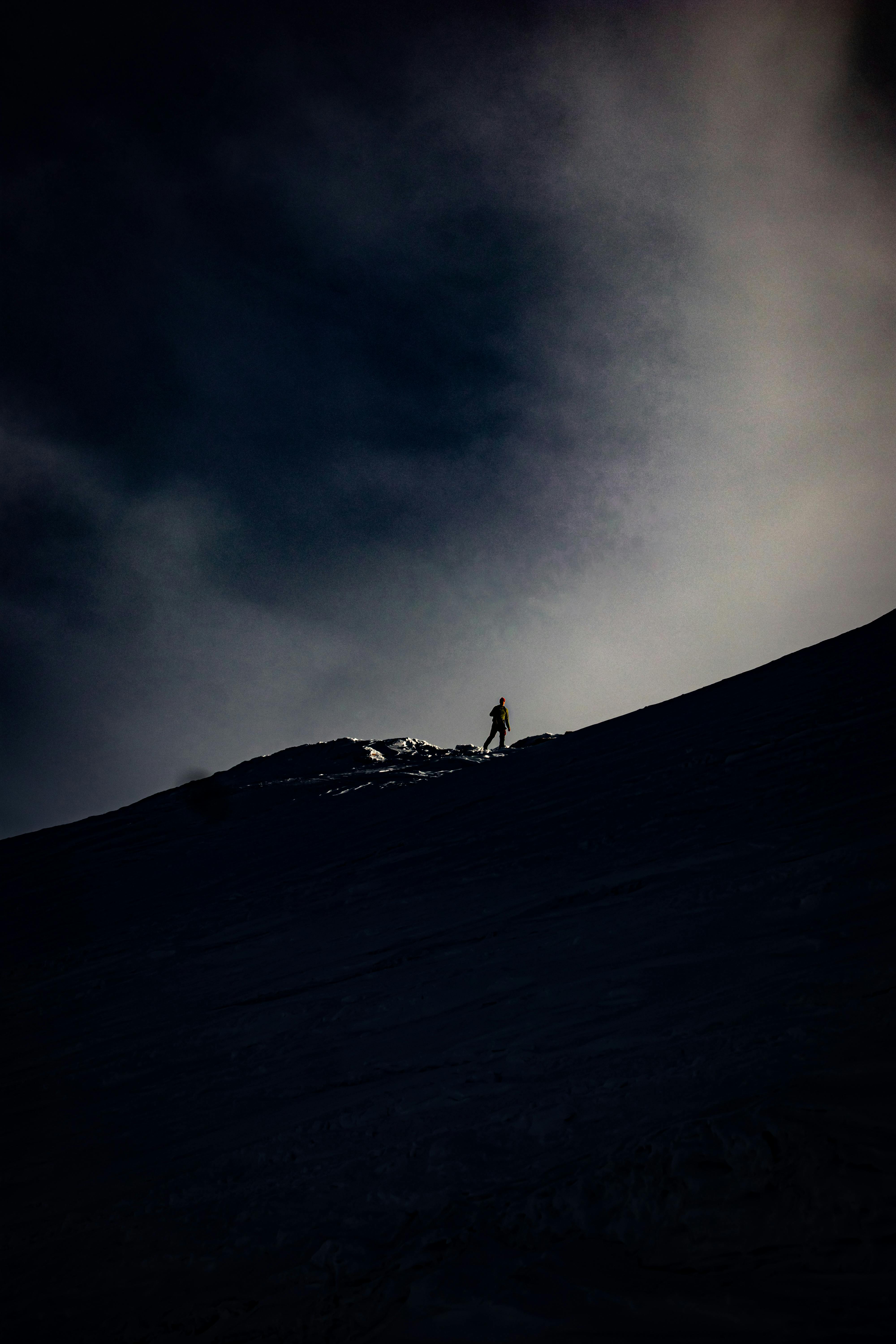 Silhouette of a lone hiker on a mountain ridge under a moody sky.