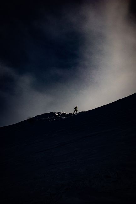 Silhouette of a lone hiker on a mountain ridge under a moody sky.