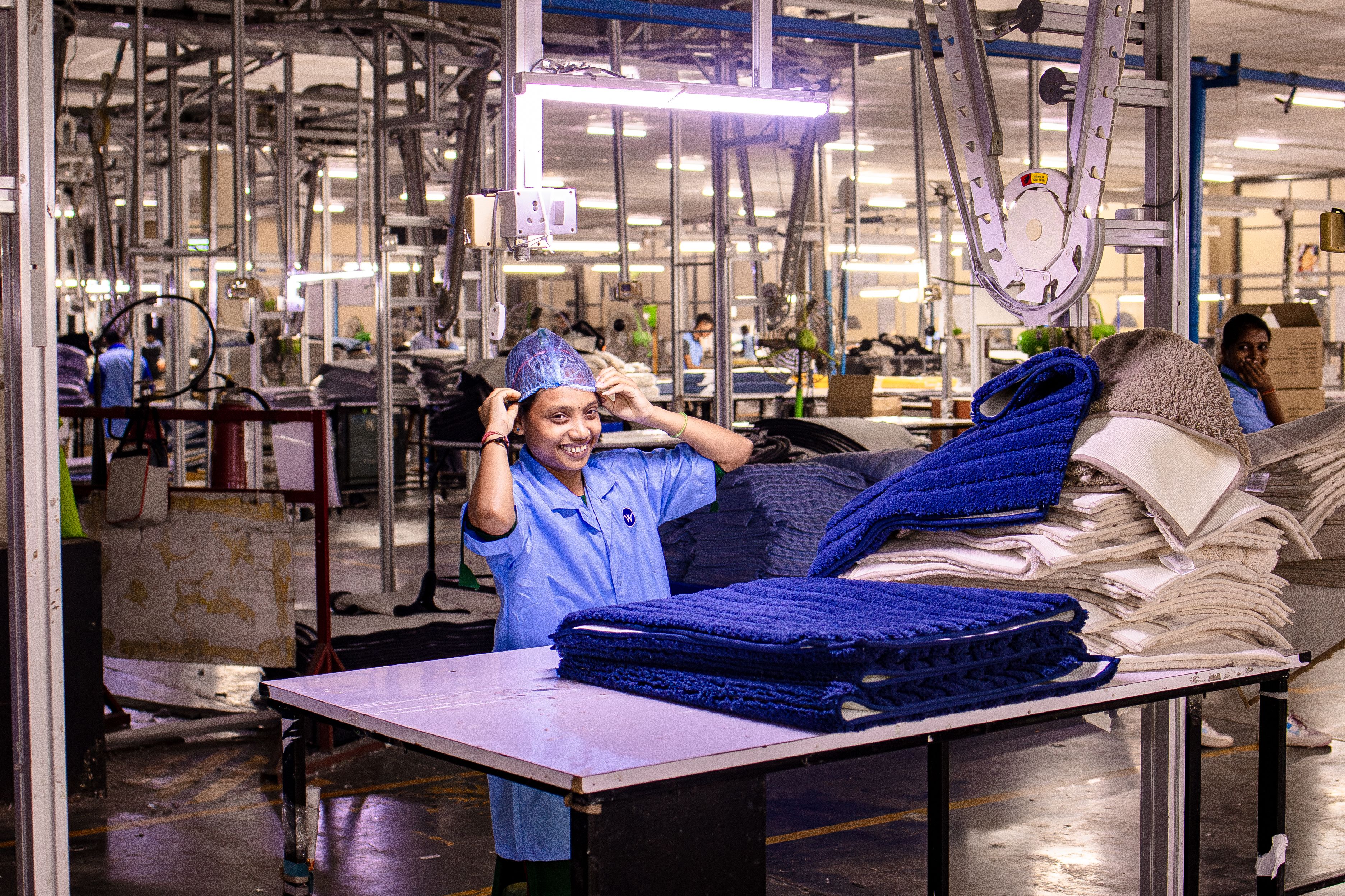 A cheerful female worker in a textile factory adjusting her cap amidst machinery and textiles.