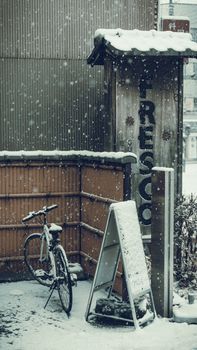 A snow-covered bicycle leans against a fence in an urban setting, creating a serene winter scene.