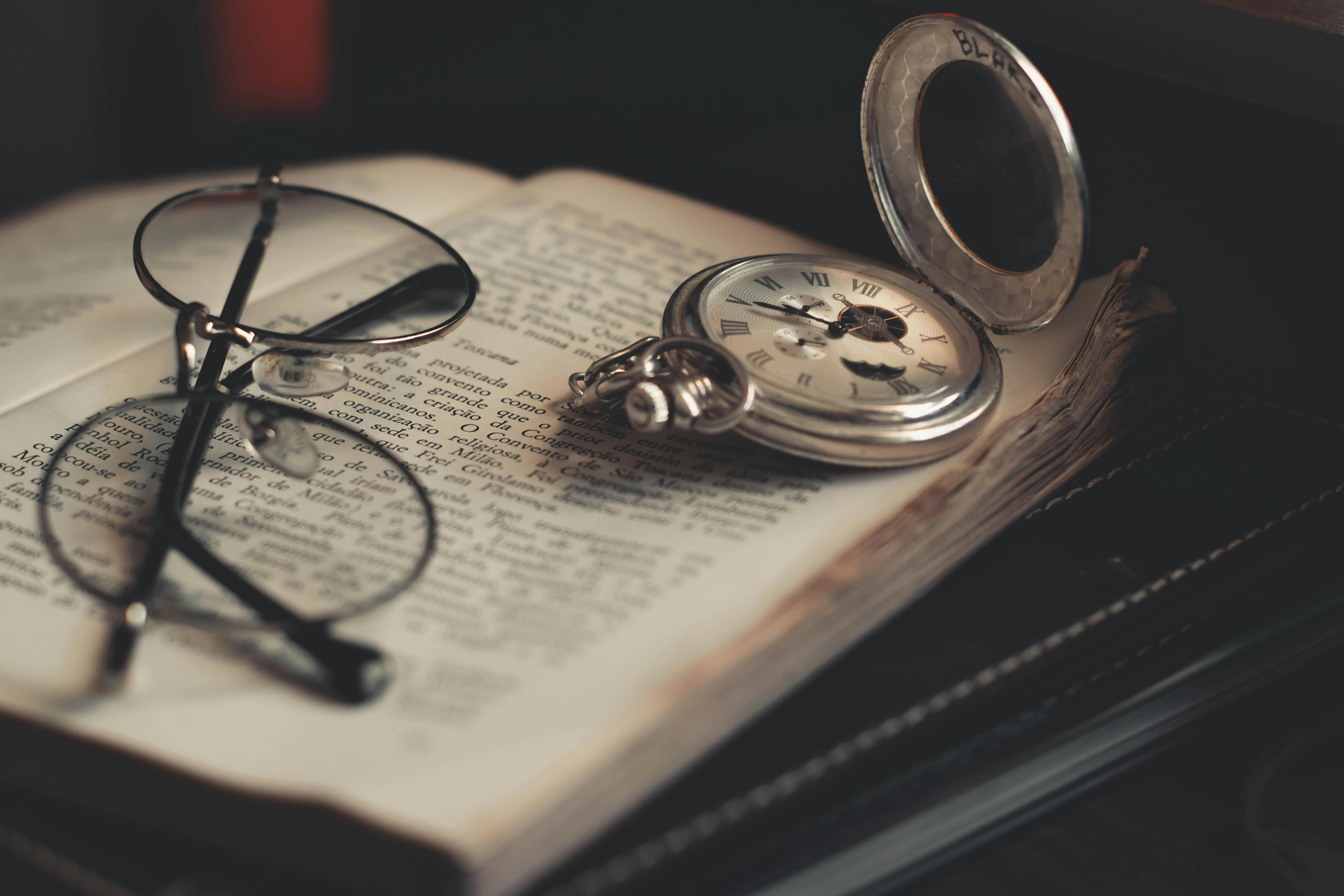 Round Silver-Colored Pocket Watch and Eyeglasses on Opened Book