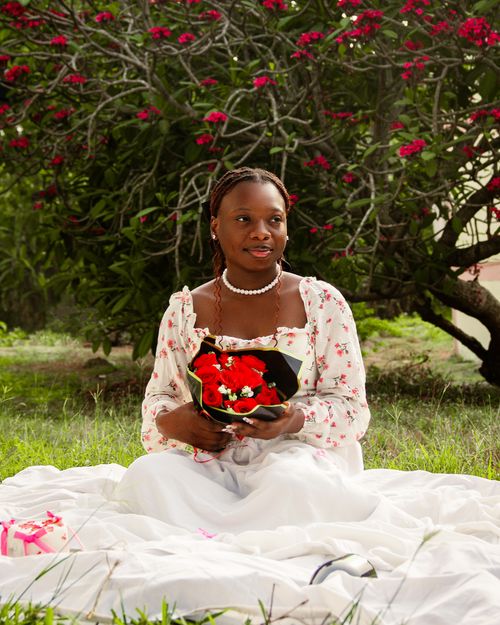 Free A woman in a floral dress holding a red bouquet, seated on a blanket outdoors. Stock Photo