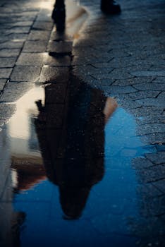 Artistic shot capturing a person's reflection in a street puddle.