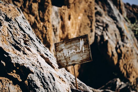 A close-up of a weathered sign in the rugged terrain of the Omani desert.