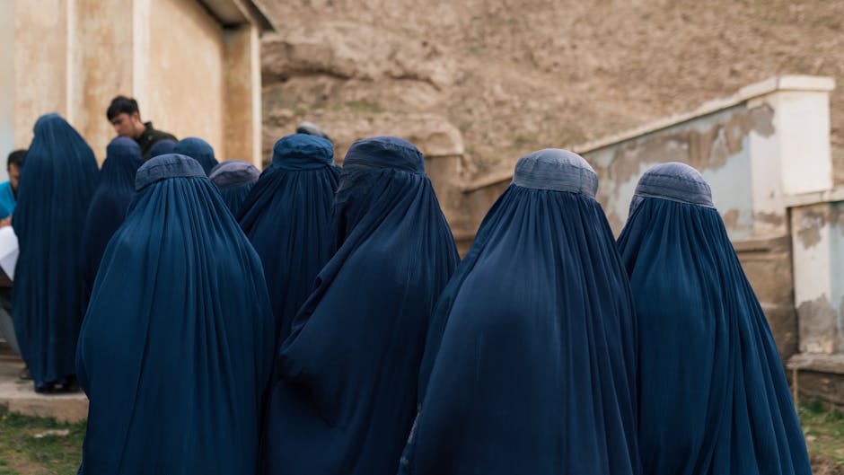 A group of women wearing traditional blue burqas walk together outdoors in Afghanistan.