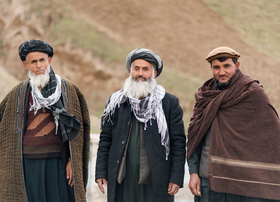 Three Afghan men in traditional attire standing outdoors, showcasing cultural attire and identity.