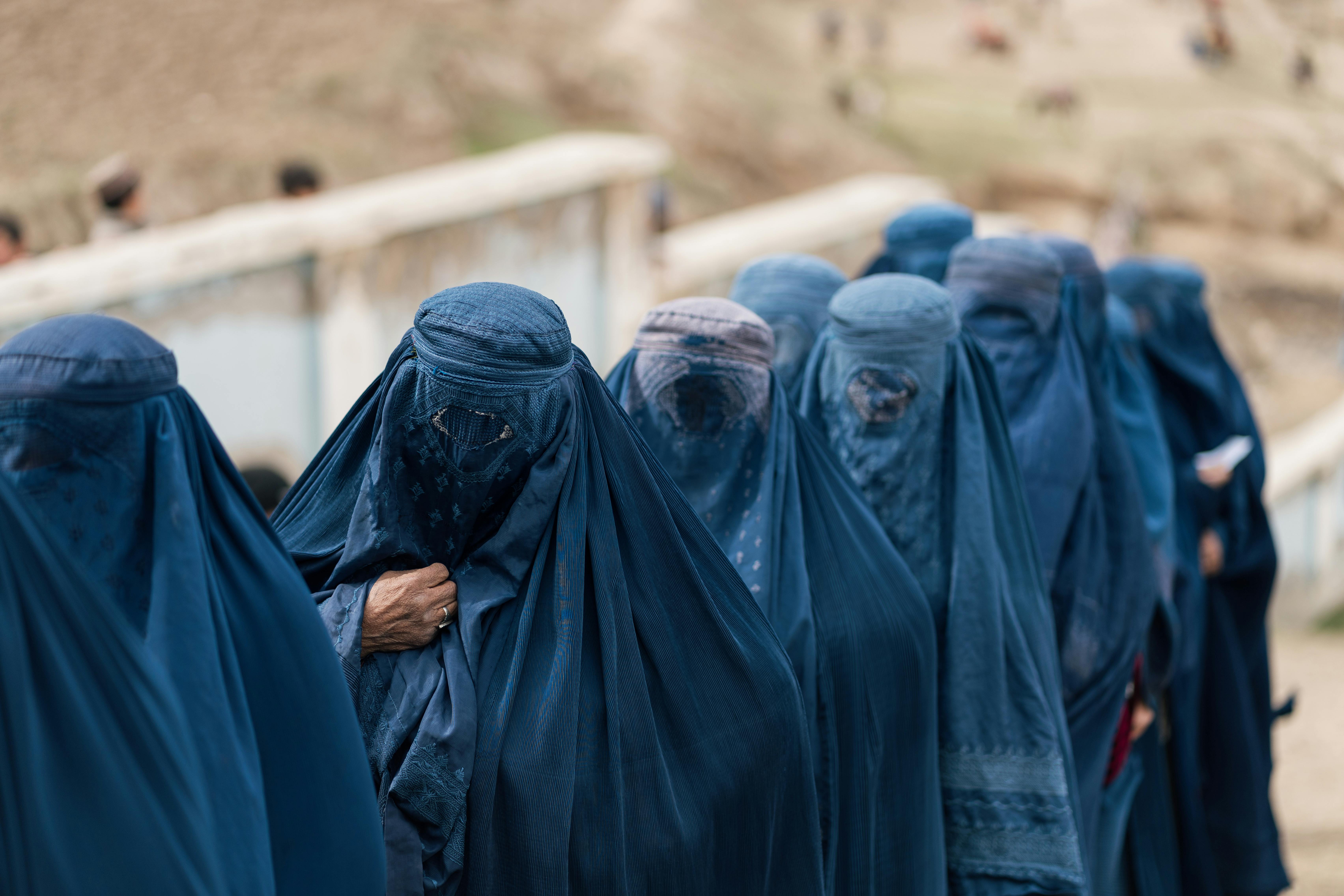 A group of women covered in blue burqas walking outdoors in Afghanistan, highlighting cultural attire.