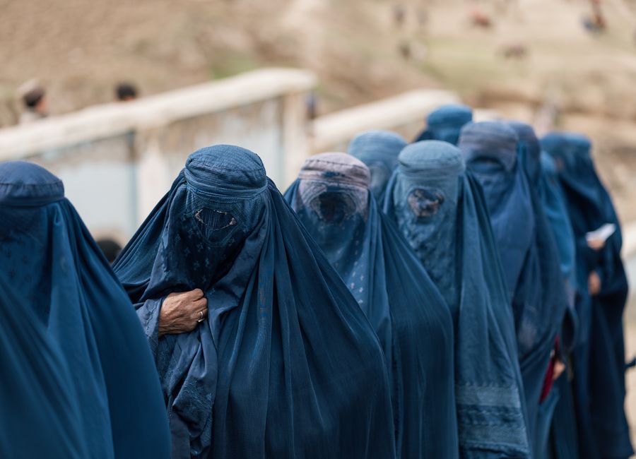 A group of women covered in blue burqas walking outdoors in Afghanistan, highlighting cultural attire.
