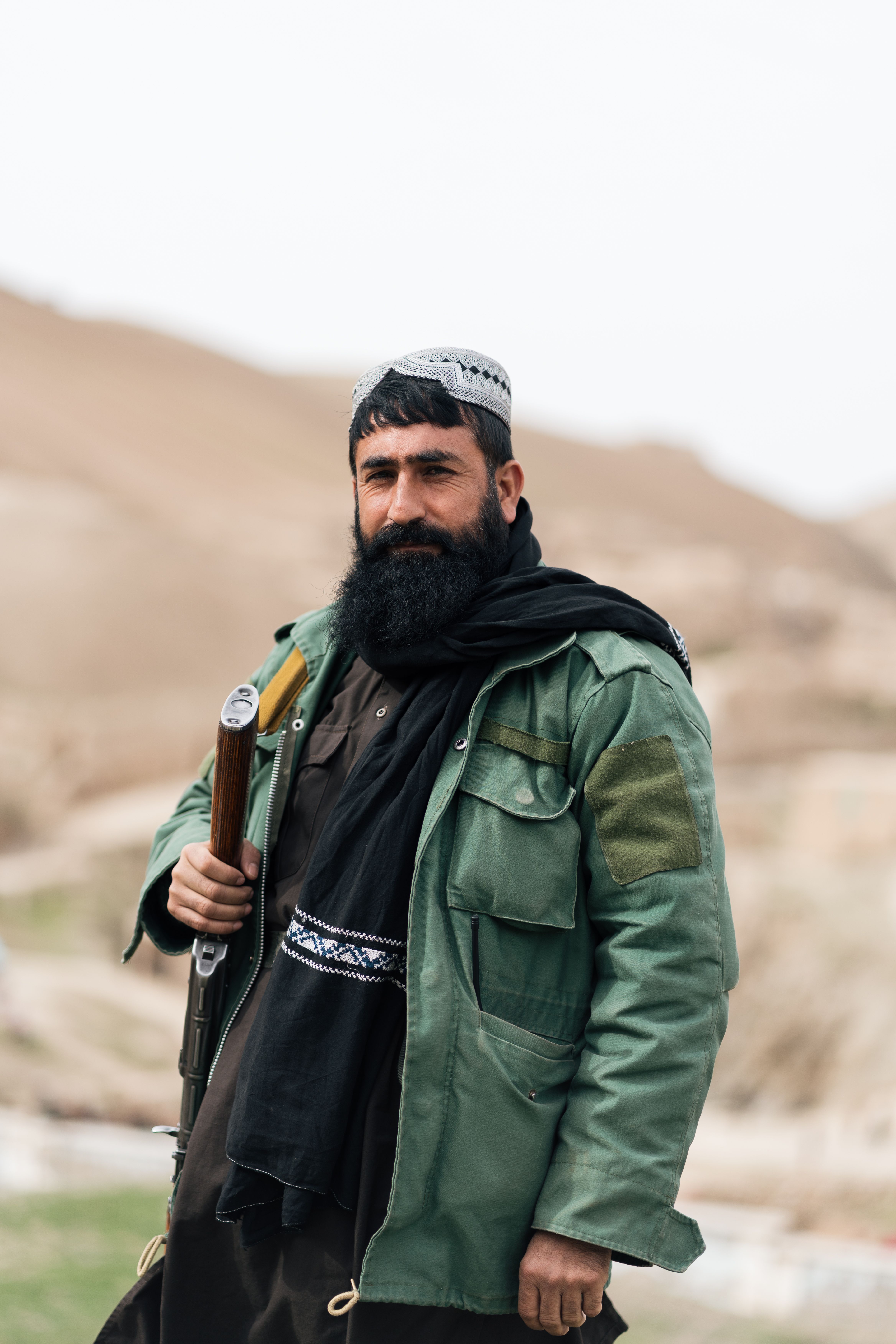 A man in traditional attire holding a rifle in rural Afghanistan, showcasing cultural elements.