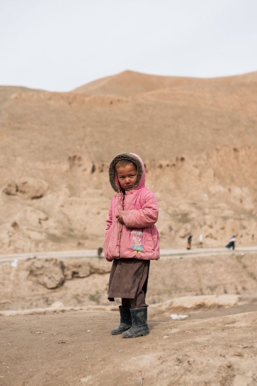 Free A young girl standing in Afghanistan's rugged terrain wearing a pink coat. Captured outdoors during the day. Stock Photo