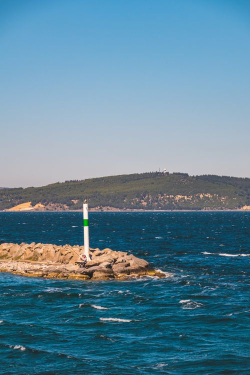 Free A picturesque view of a coastal islet with a small lighthouse and vast blue sea under a clear sky. Stock Photo
