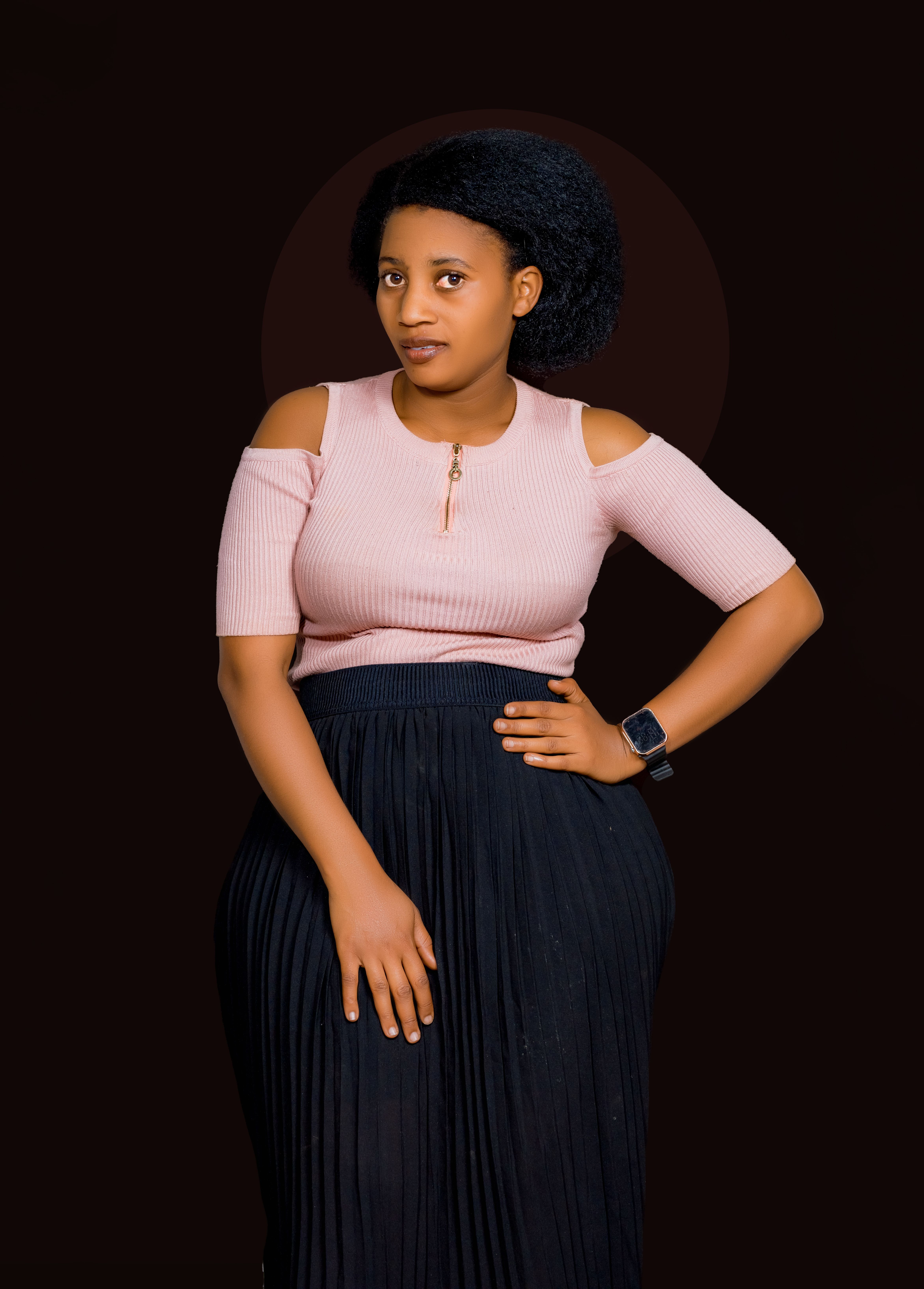 Stylish young woman poses confidently with hand on hip. Studio shot with a dark background.