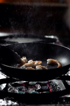 Close-up of shrimp cooking in a black pan, showcasing culinary preparation.