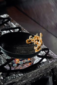 Sausages cooking on a frying pan over a gas stove in a kitchen setting.