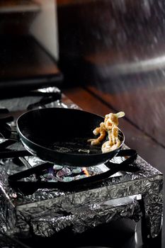 Close-up of seafood cooking on a black pan over a gas stove, showcasing culinary techniques.