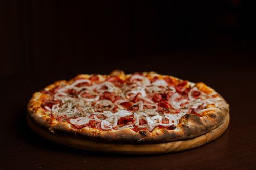 Free Close-up of a pepperoni pizza with onions on a wooden table, perfect for food lovers. Stock Photo