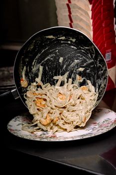Delicious creamy shrimp pasta being served onto a decorative plate from a pan.