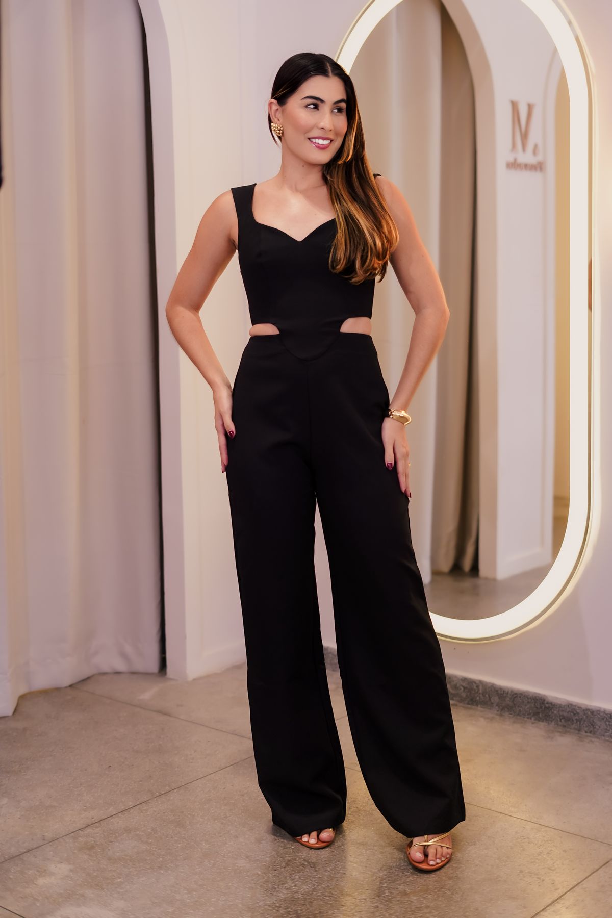 Woman in a black wide-leg jumpsuit with cutouts in a bright room, an evening cocktail wedding guest outfit