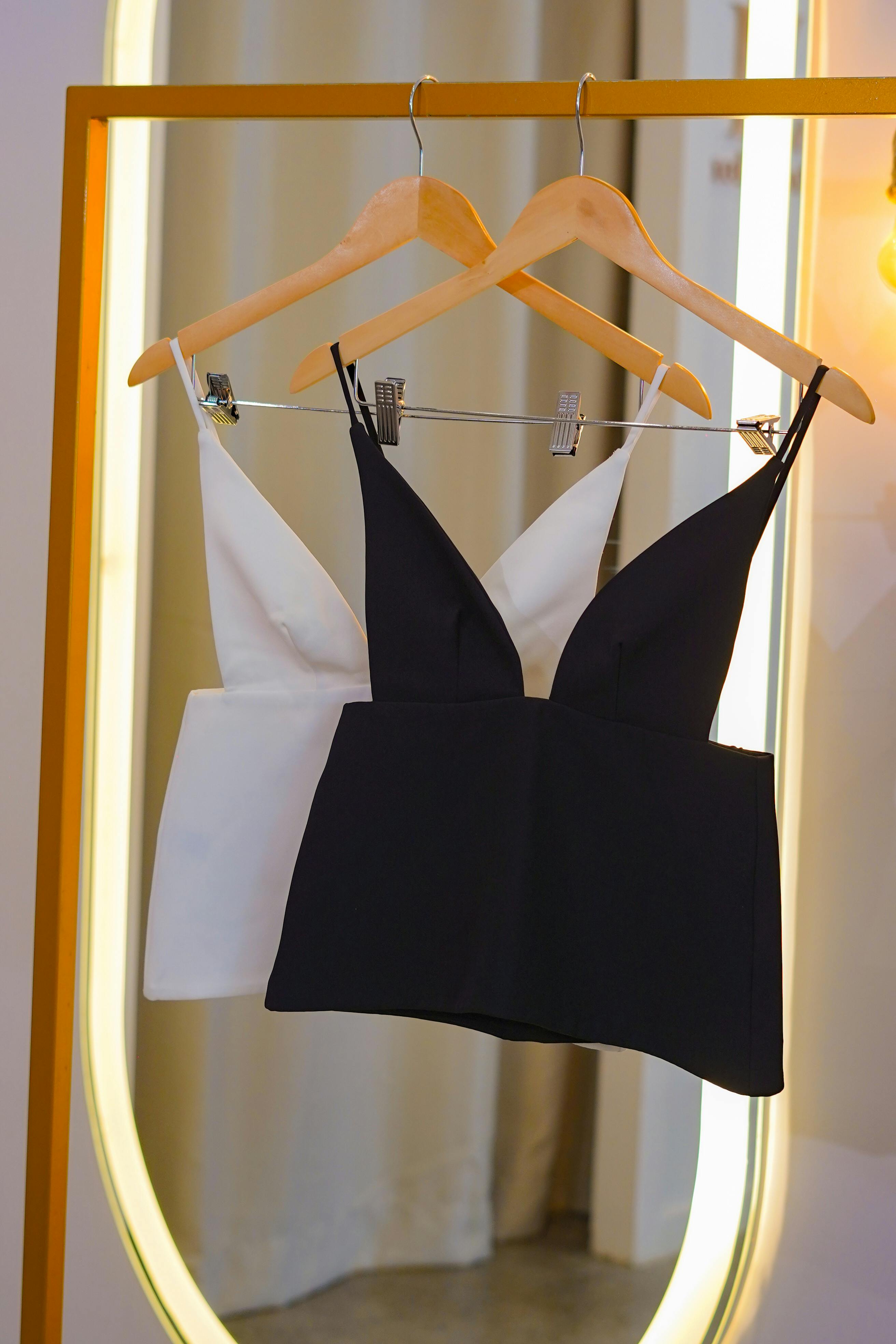 Stylish black and white tops on hangers in front of a golden mirror indoors.