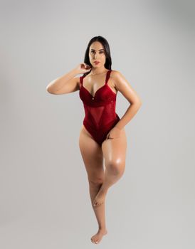 A confident woman poses in a vibrant red lingerie set against a neutral background, showcasing elegance and style.