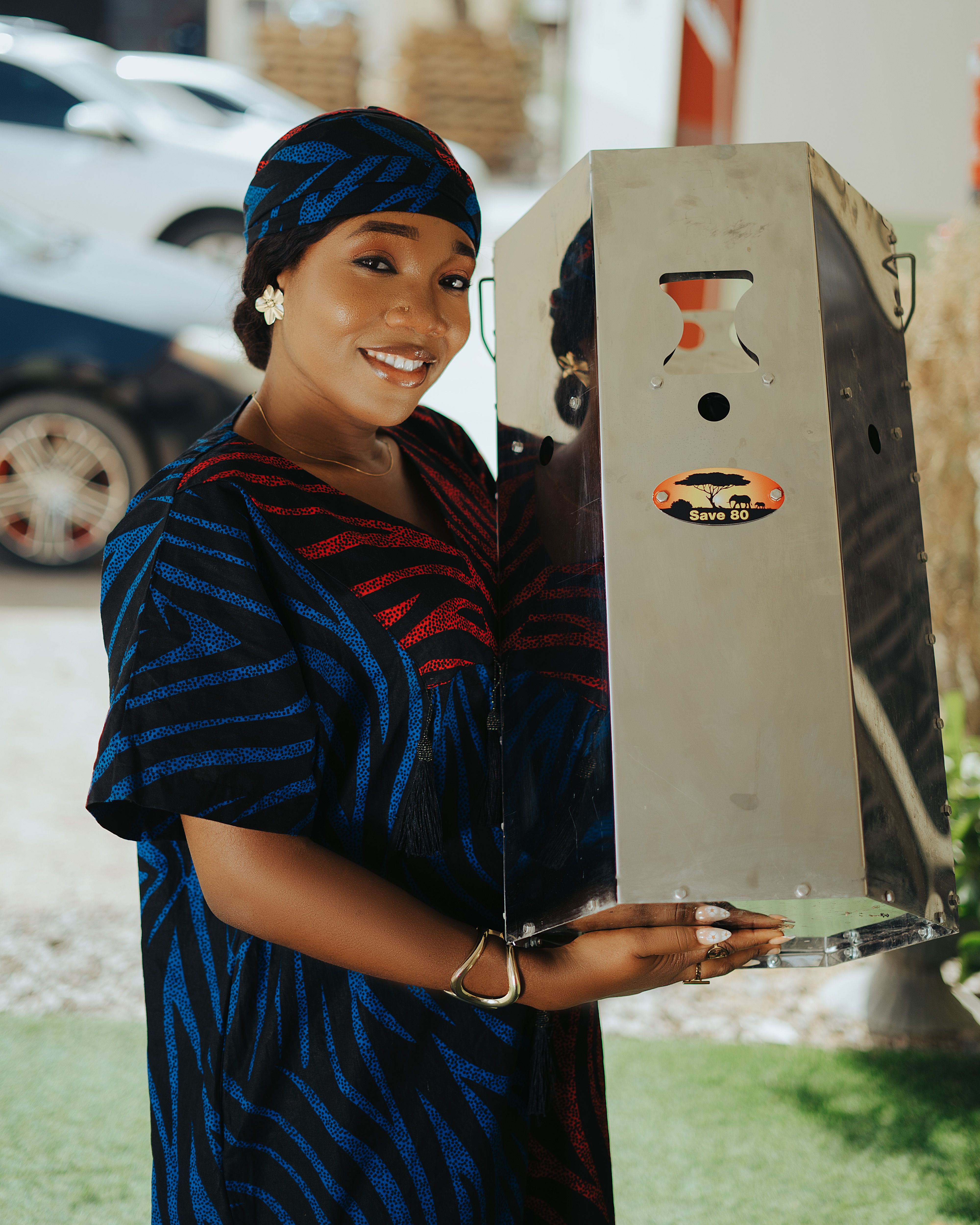 Smiling woman in vibrant dress holding a metal product outdoors.