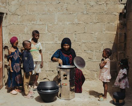 An African woman cooking outdoors surrounded by children showcasing traditional lifestyle.