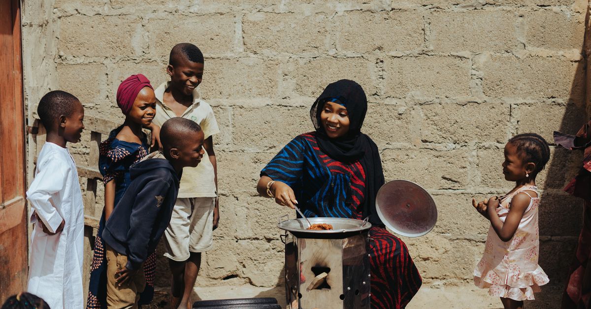African grandmother teaching young woman how to cook traditional stew in outdoor kitchen